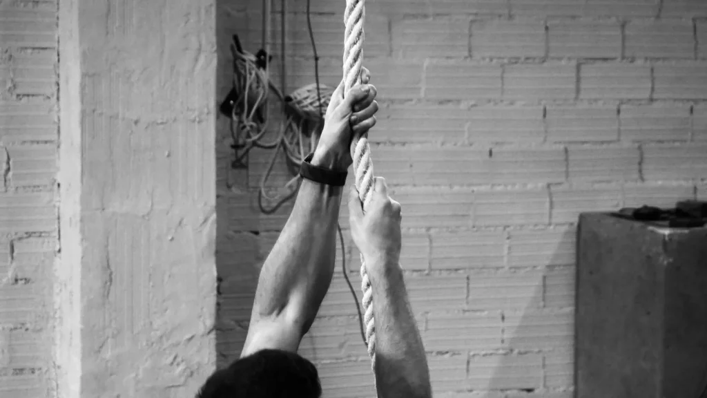 Detalle en blanco y negro de manos agarrando una cuerda de trepa durante entrenamiento para oposiciones de bomberos en S4S Preparación Física, Madrid